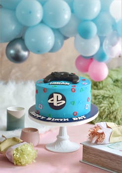 A PlayStation-themed birthday cake on a stand with colorful balloons and decor.