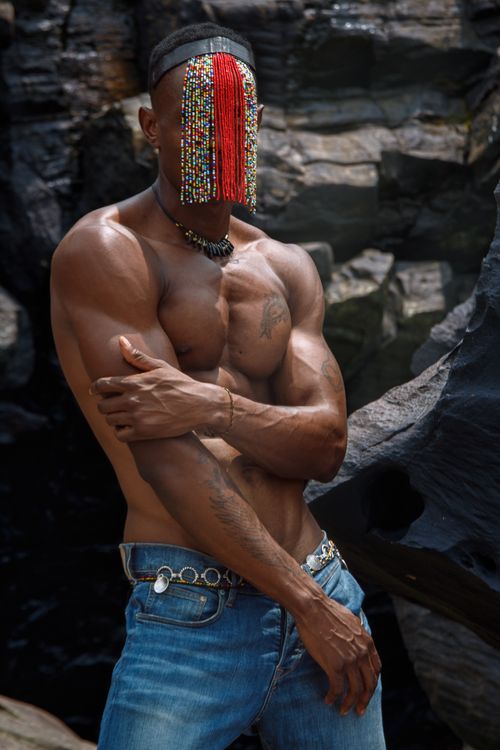 Free Striking portrait of a muscular man wearing a colorful beaded mask, standing against rocky background. Stock Photo