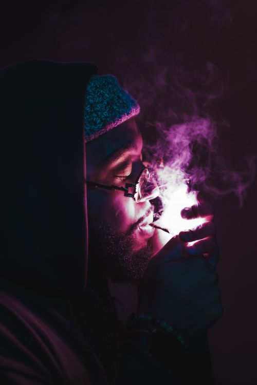 Free A dramatic low-light portrait of a man enjoying a smoke, featuring vibrant smoke and eyeglasses. Stock Photo