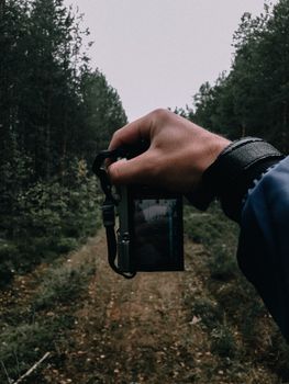 Hand holding a camera capturing a forest scene, showcasing outdoor photography and nature exploration.