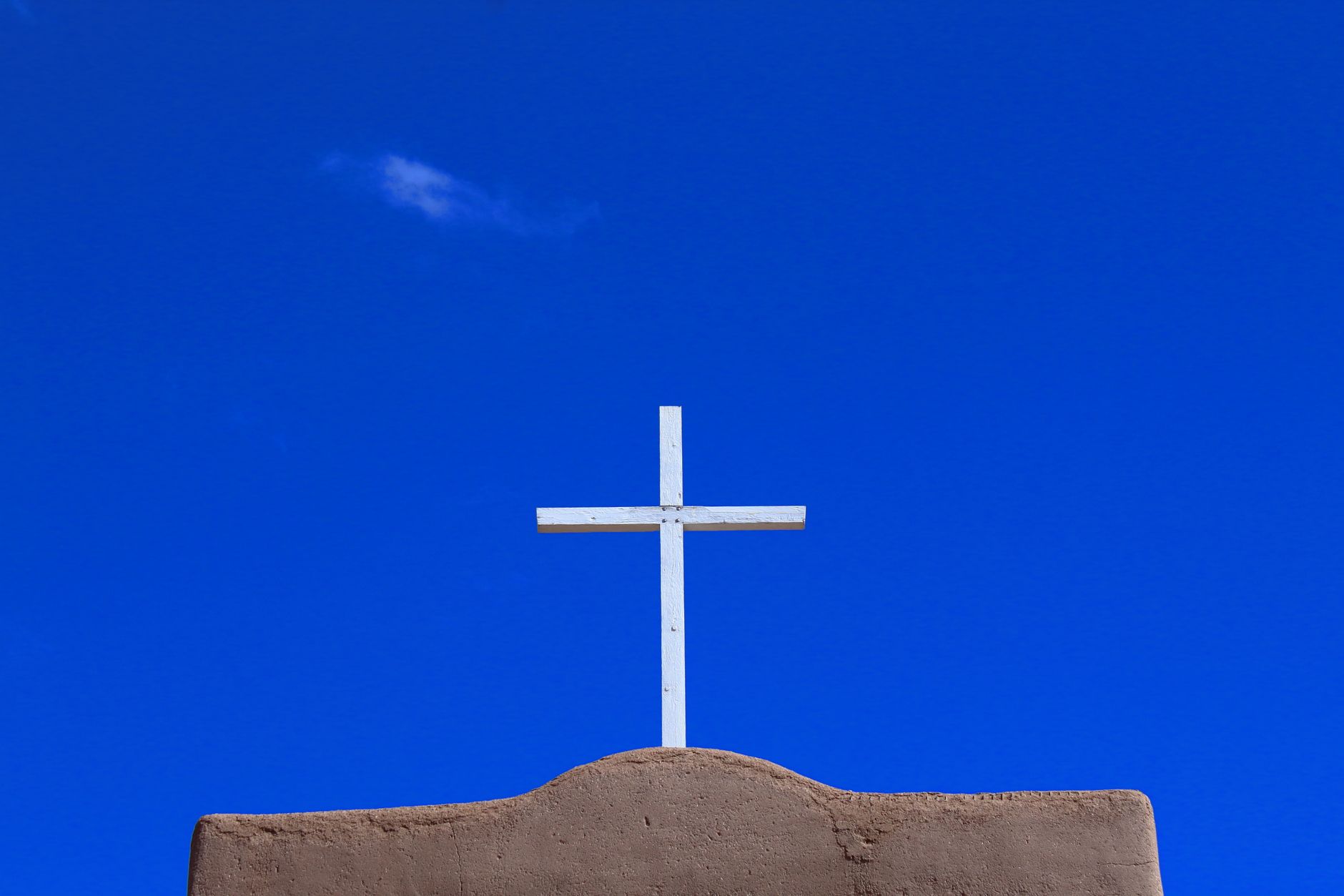 A white cross on adobe building at Santa Fe, NM, silhouetted against a clear blue sky.