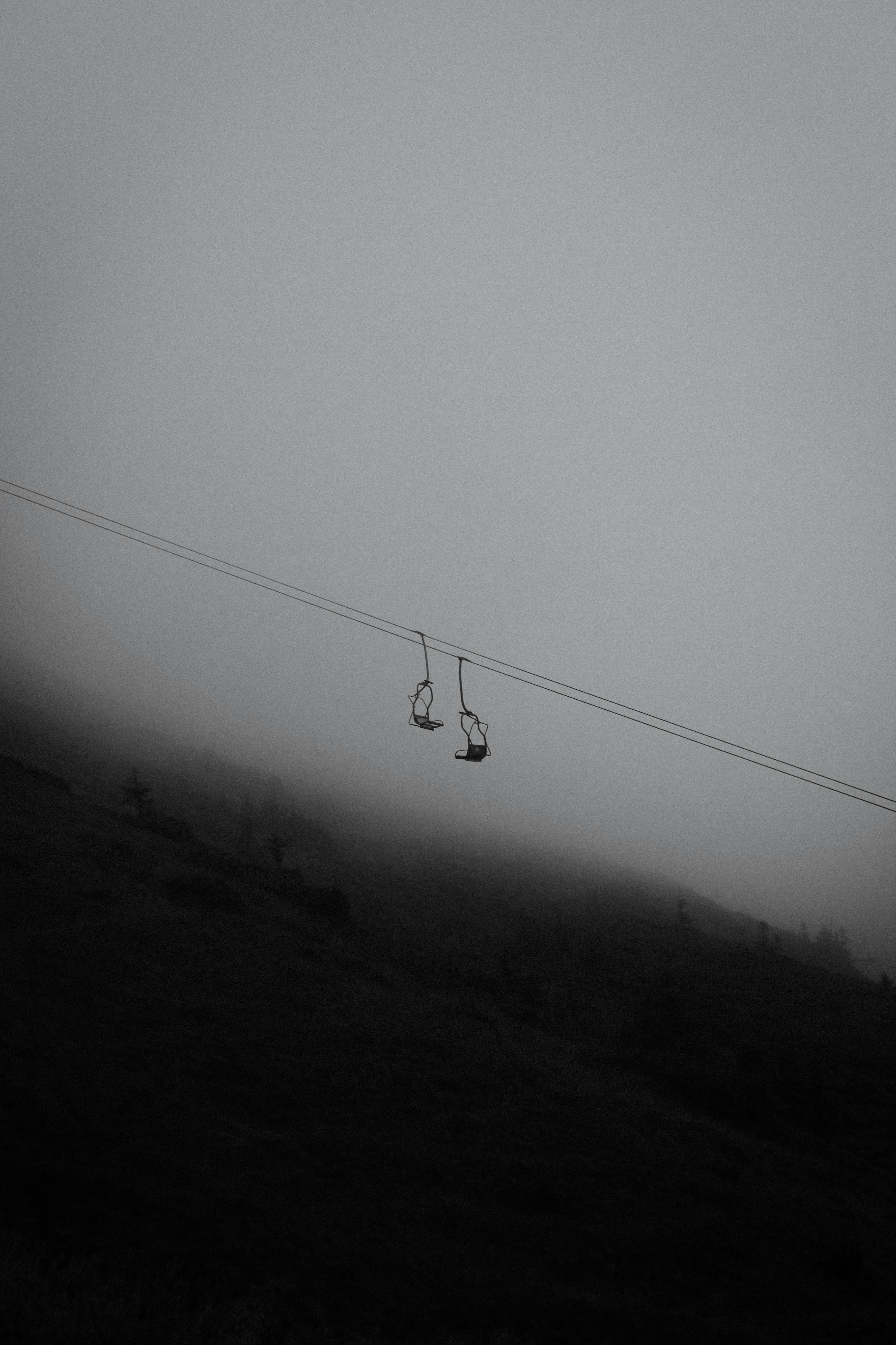 A stark black and white image of cable cars amidst fog on a mountain at dusk, creating a mysterious atmosphere.