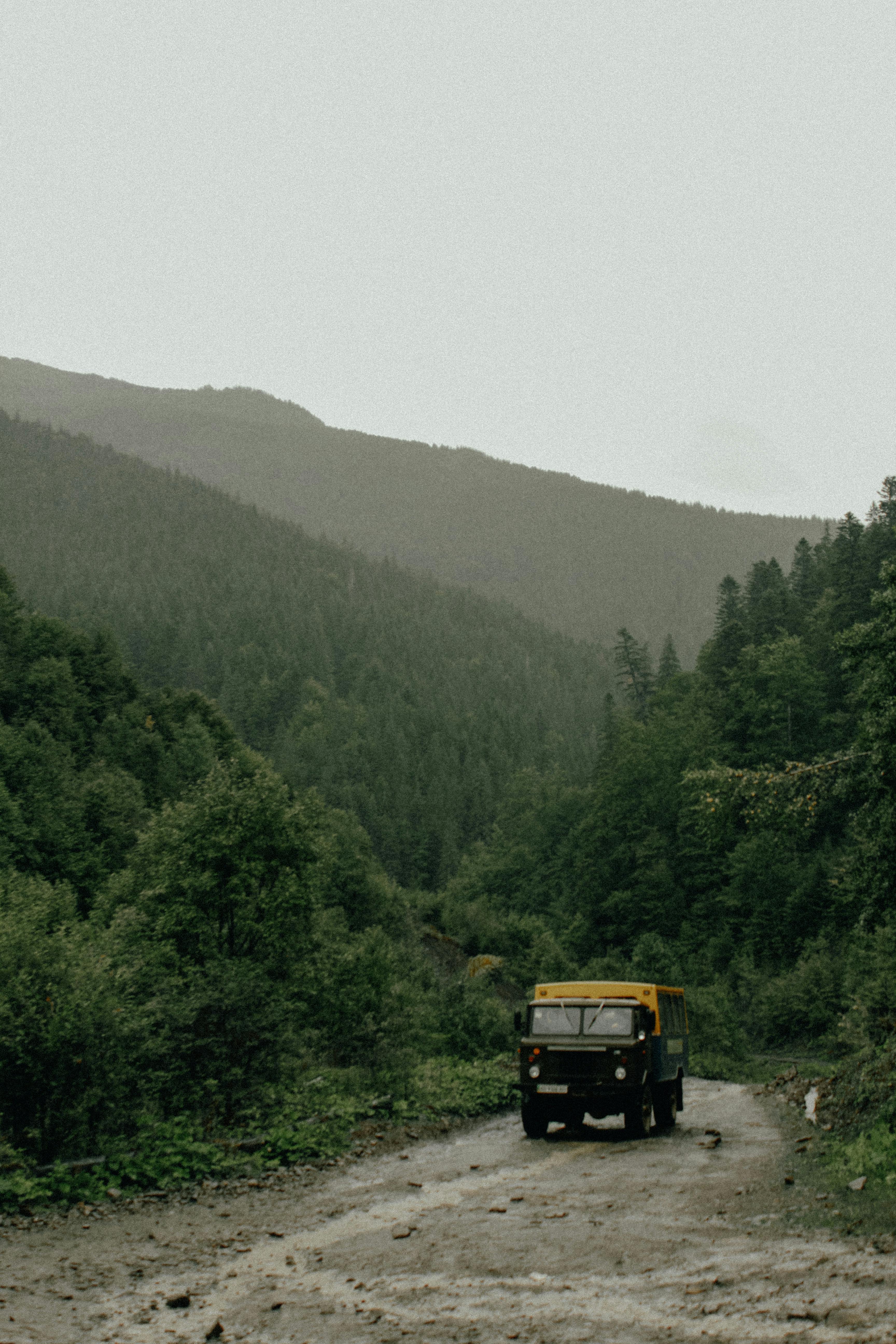 A rugged truck traversing a muddy dirt road surrounded by lush, mountainous forest terrain.