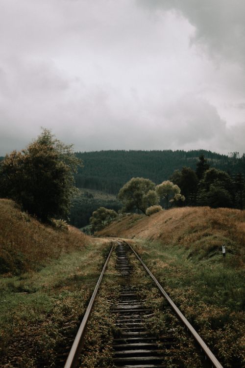 Free A peaceful railway track cutting through lush green hills under a cloudy sky, evoking tranquility. Stock Photo