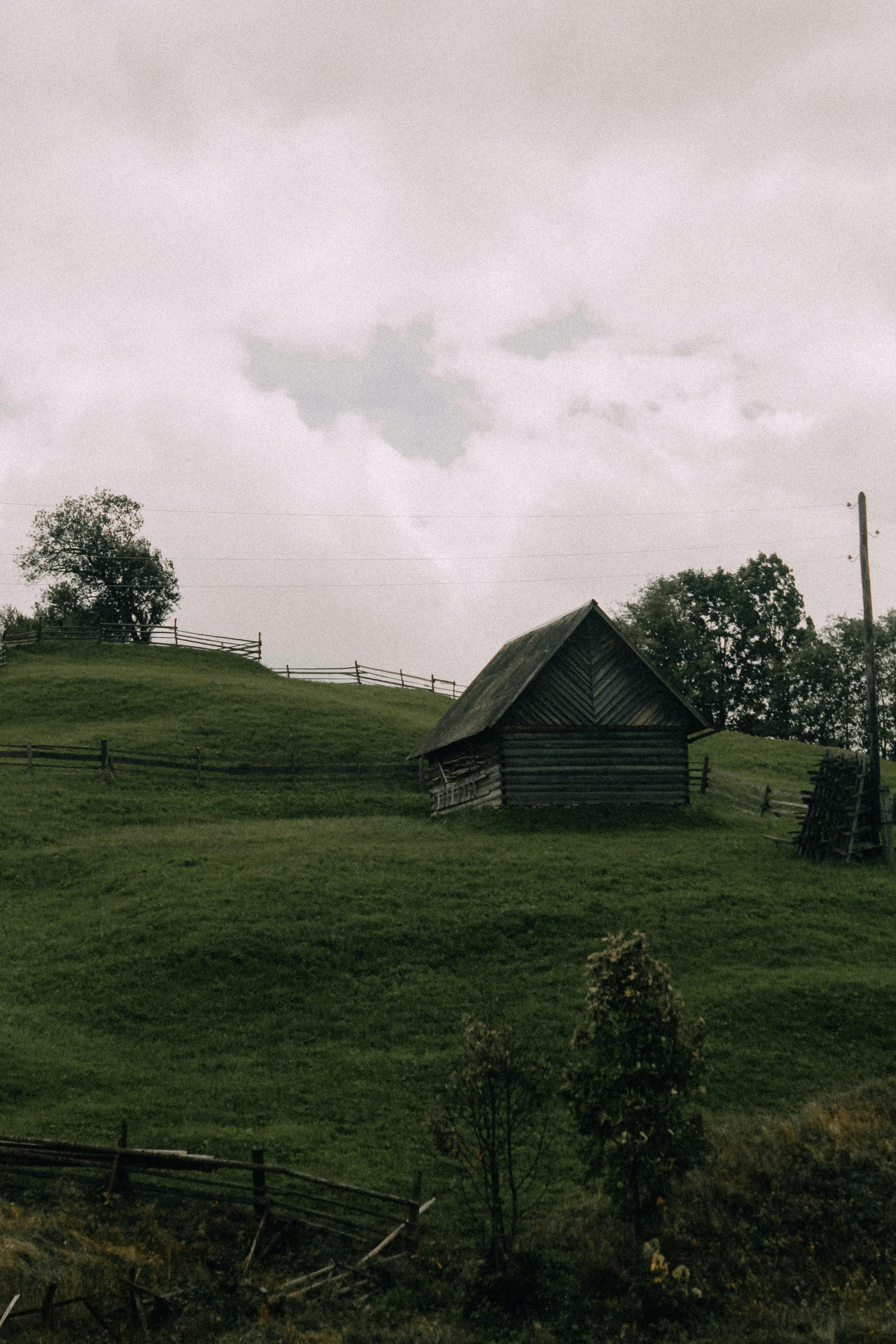 Picturesque view of a wooden cabin on a grassy hillside under a cloudy sky, offering a serene nature escape.
