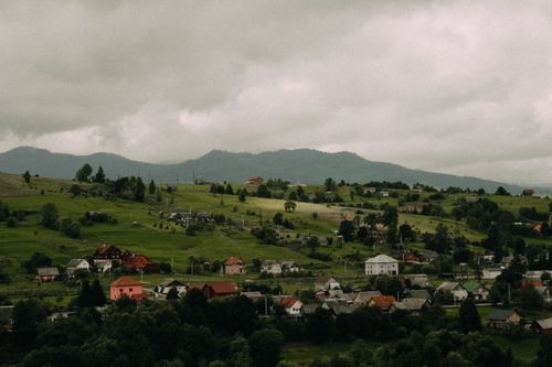 Free Explore the serene beauty of a picturesque mountain village surrounded by lush green landscapes and cloudy skies. Stock Photo