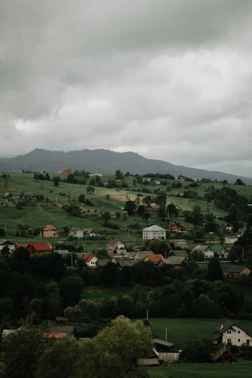 Free Picturesque mountain village scene with lush greenery and looming clouds creating a serene environment. Stock Photo
