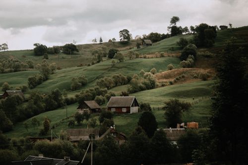 Free Charming rural landscape featuring lush green hills and rustic cottages under a cloudy sky. Stock Photo