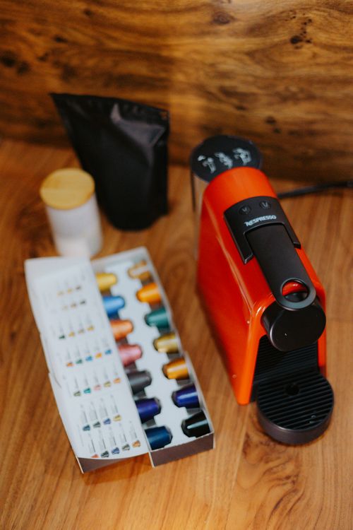 Free Vertical shot of a red coffee machine with assorted capsules and accessories on a wooden surface. Stock Photo