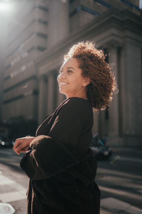 Free A joyful woman with curly hair enjoying a sunny day in the city. Stock Photo