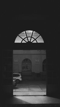 A captivating black and white photo of a shadowy arched doorway leading to a sunlit urban scene.