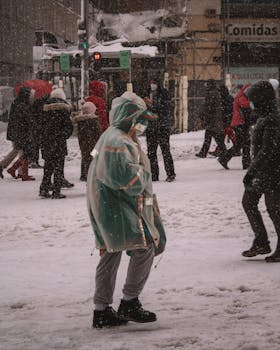 A bustling street scene with people walking through falling snow in winter, wearing warm clothes and masks.