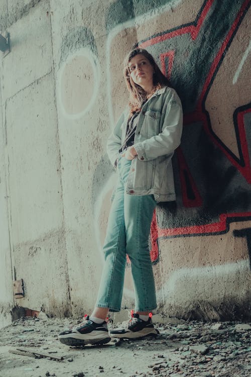 Girl in Denim Jacket and Blue Jeans Leaning on Graffiti Wall