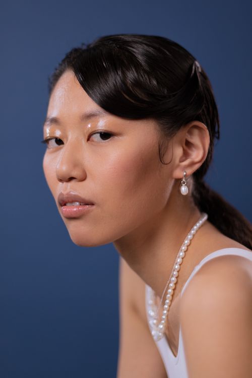 Free Stylish portrait of a woman wearing pearl necklace and earrings against a blue backdrop. Stock Photo