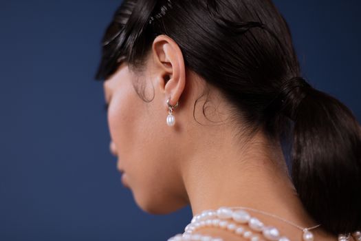 Close-up of a woman wearing pearl jewelry against a blue background.