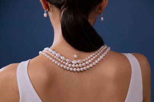 Free Elegant pearl necklace adorned on a woman's neck against a blue backdrop. Stock Photo