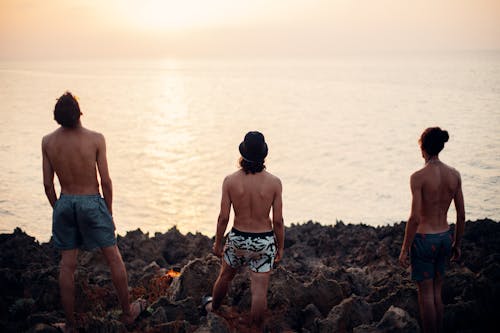 Back View of Topless Men Standing on Rocky Shore