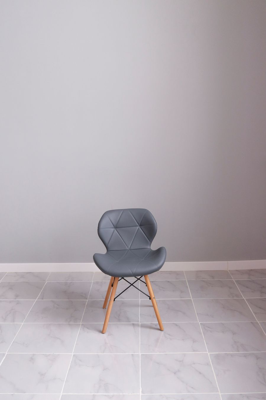 Moulded grey chair on light wooden legs against a plain wall — photo by Леся Терехова on Pexels