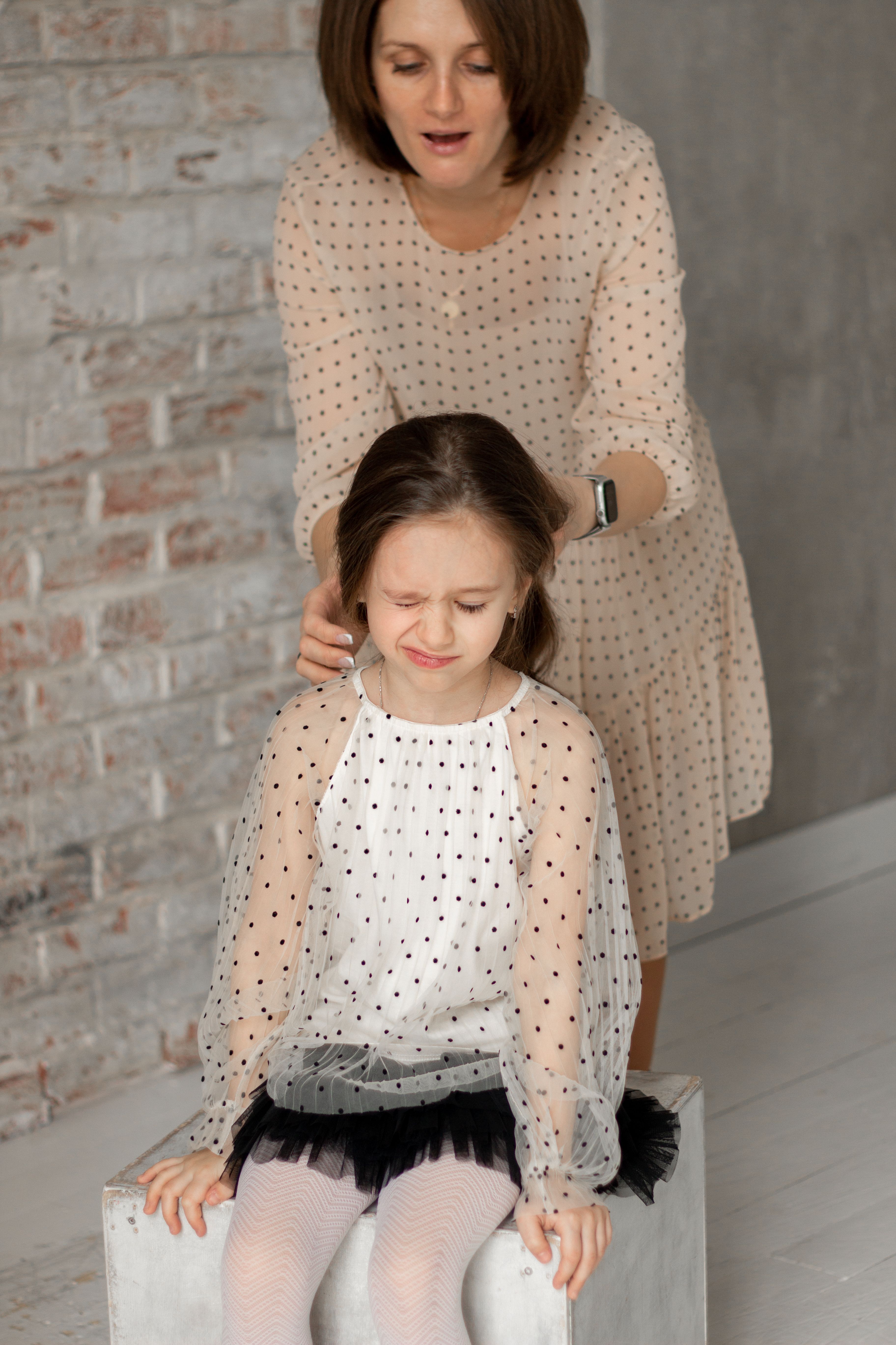 Mother tenderly fixes her daughter's hair, showcasing love and bonding.