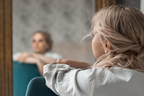 Free A contemplative woman with blonde hair gazes into a mirror, capturing a reflective indoor scene. Stock Photo