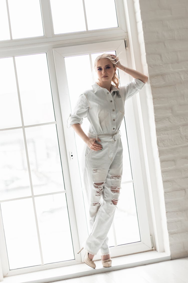 Woman In White Jumpsuit Standing By A Glass Window