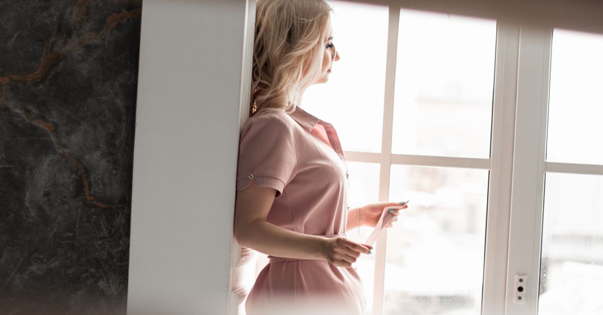 A thoughtful adult looking out a window with a notebook