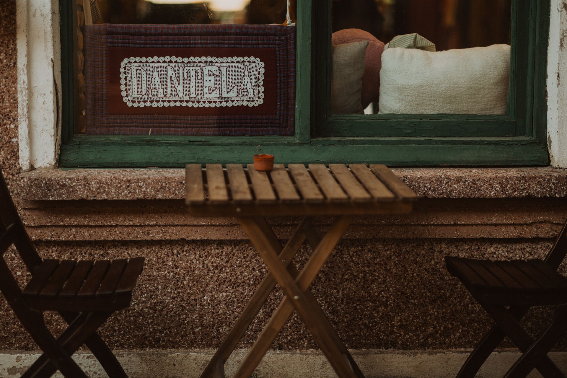 Rustic outdoor seating area with wooden furniture by a vintage window, ideal for a cozy coffee break.