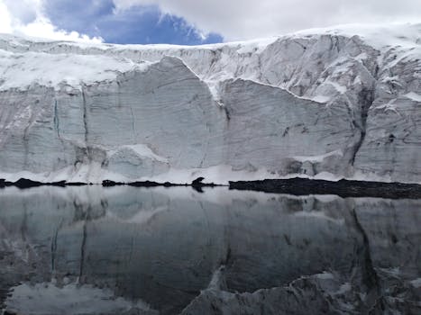 A stunning glacier mirrors in calm water under a blue sky, showcasing serene natural beauty.
