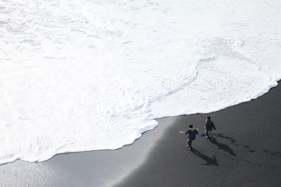 Two children enjoy the waves at Iceland's remarkable black sand beach.