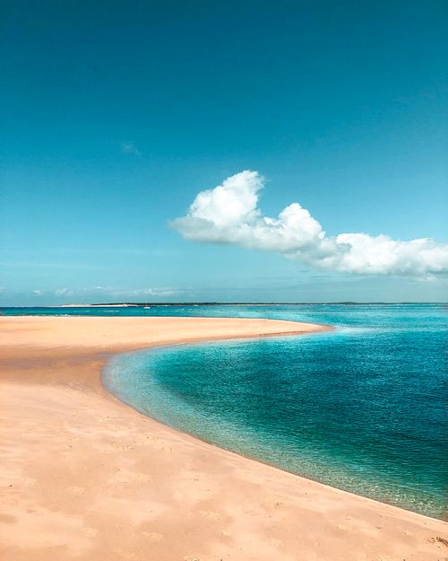 Free Serene sandy beach with clear blue ocean and fluffy clouds on a sunny day. Stock Photo
