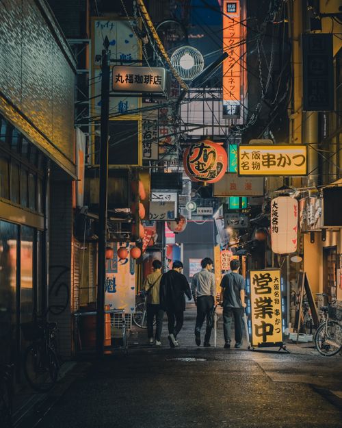 Free Four friends walking through a lively Asian street filled with neon signs at night. Stock Photo