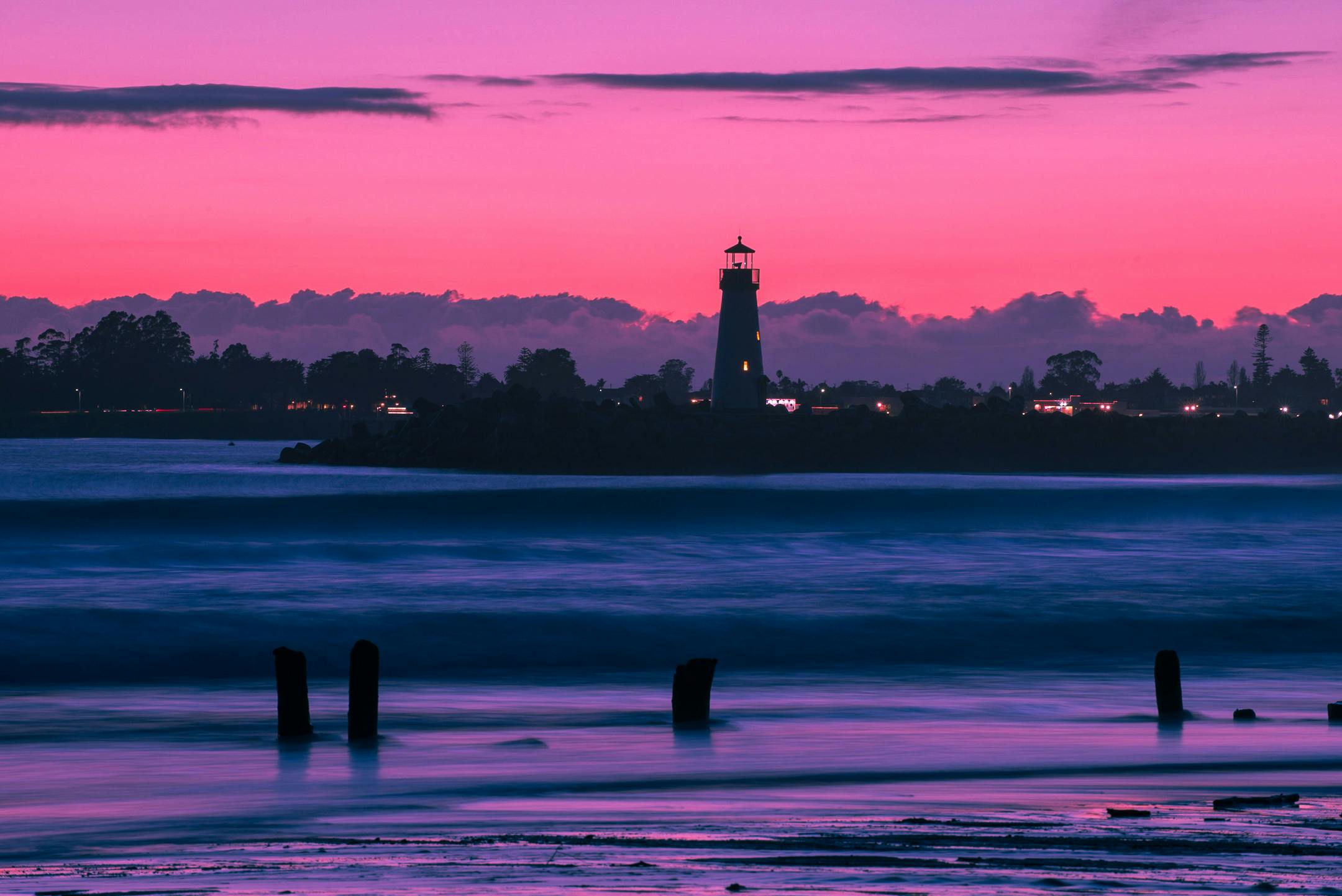 A breathtaking view of a lighthouse silhouette against a vibrant sunset sky over a calm ocean.