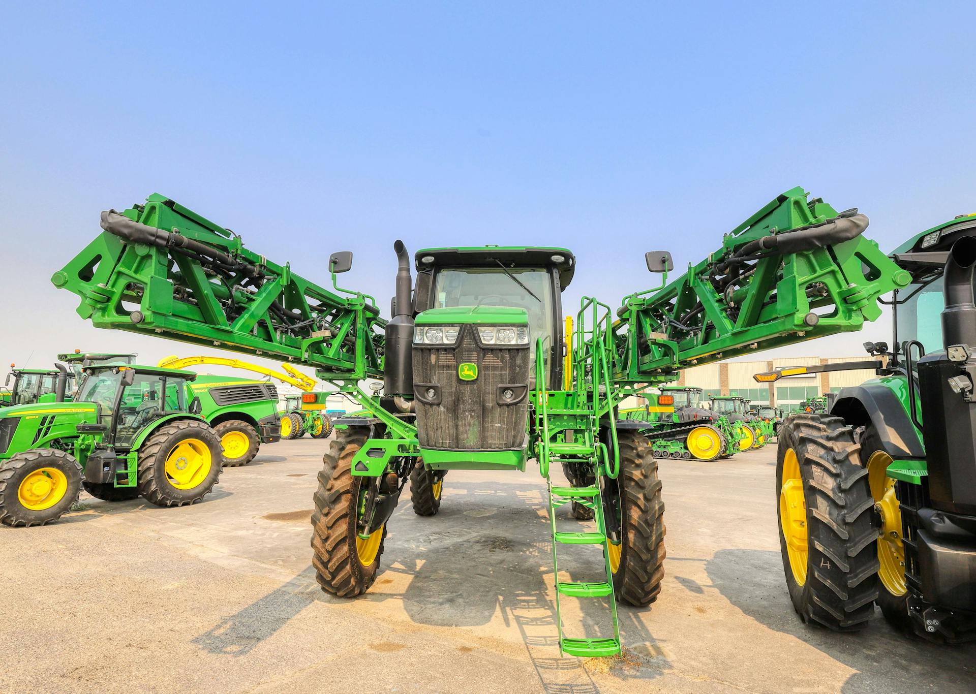 A green agricultural tractor with extended arms displayed outdoors under a blue sky in Burley.