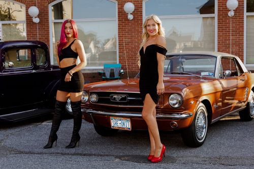 Free Two women in black outfits pose confidently with a classic Ford Mustang, showcasing elegance and style. Stock Photo