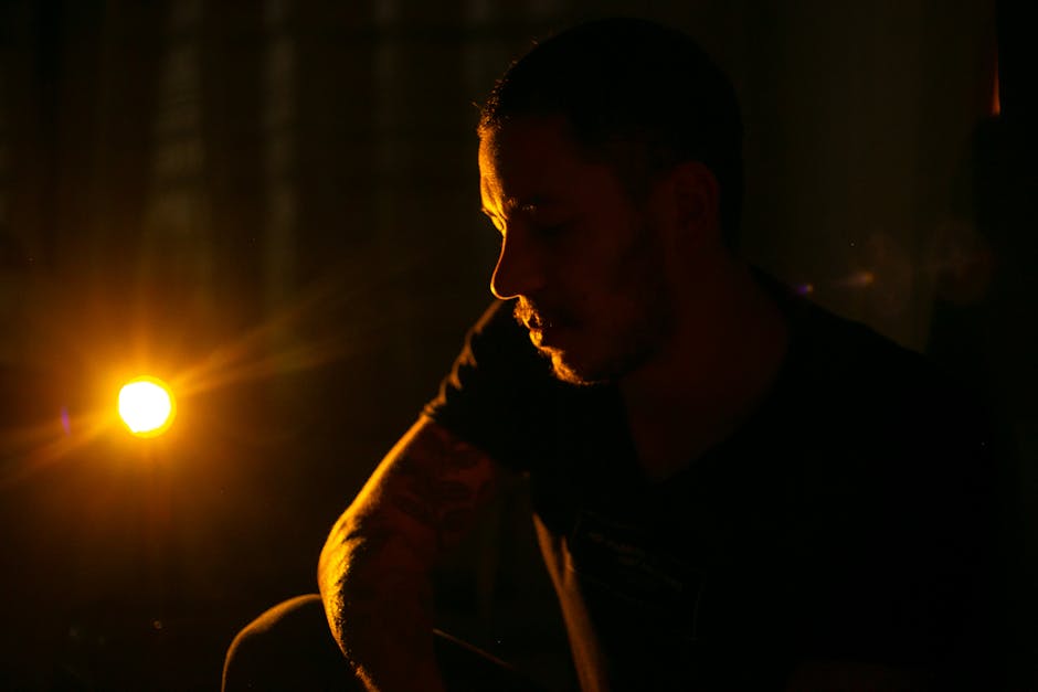 Artistic portrait of a man captured in dramatic low light, emphasizing emotion and shadow.