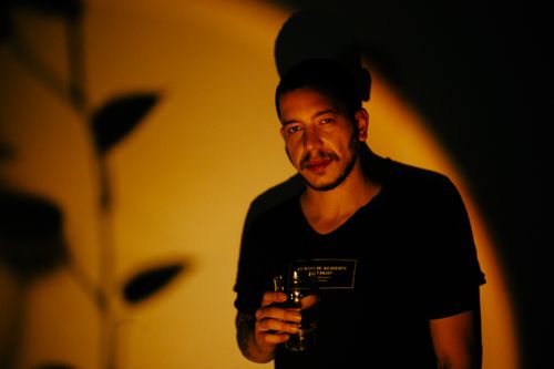 Free A man holding a drink, illuminated by a spotlight, creating dramatic shadows. Stock Photo