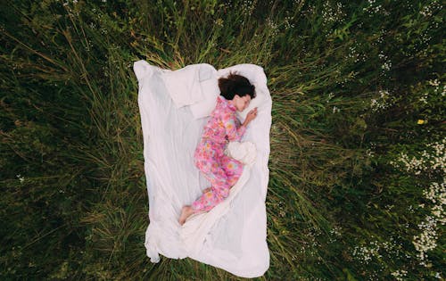 Free Woman in Pajamas Sleeping on White Blanket on Grass Field Stock Photo