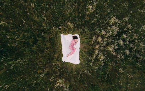 Woman in Pajamas Sleeping on White Blanket on Grass Field