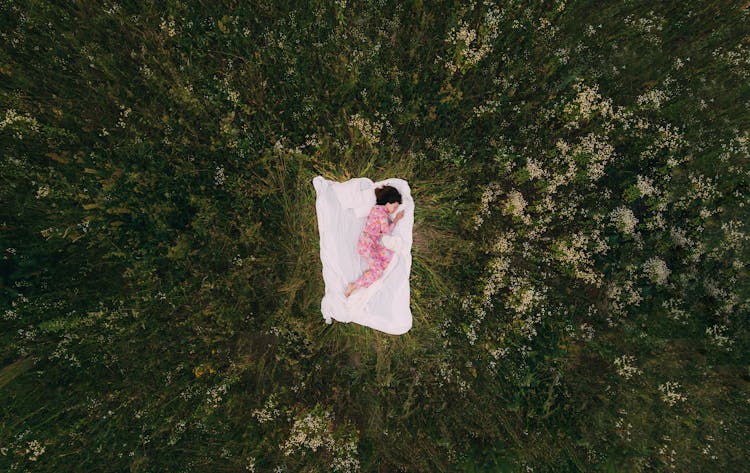 Woman In Pajamas Sleeping On White Blanket On Grass Field