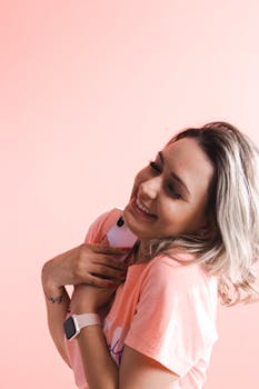 Happy woman hugging her smartphone, smiling against a pink studio background.