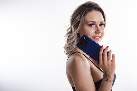 Portrait of a smiling woman posing with a blue smartphone against a white background.
