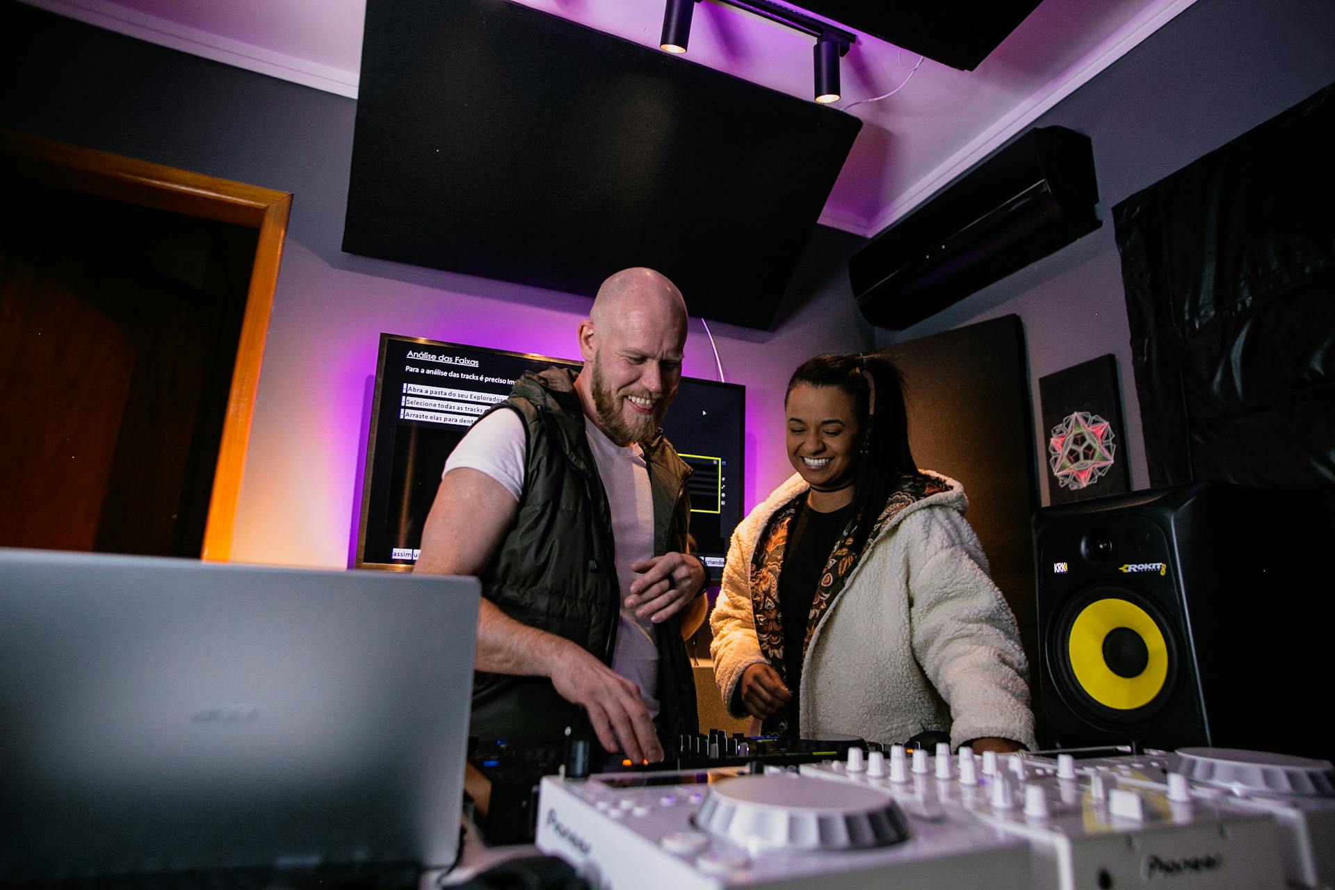 A diverse duo of DJs collaborating and smiling while producing music in a modern studio.