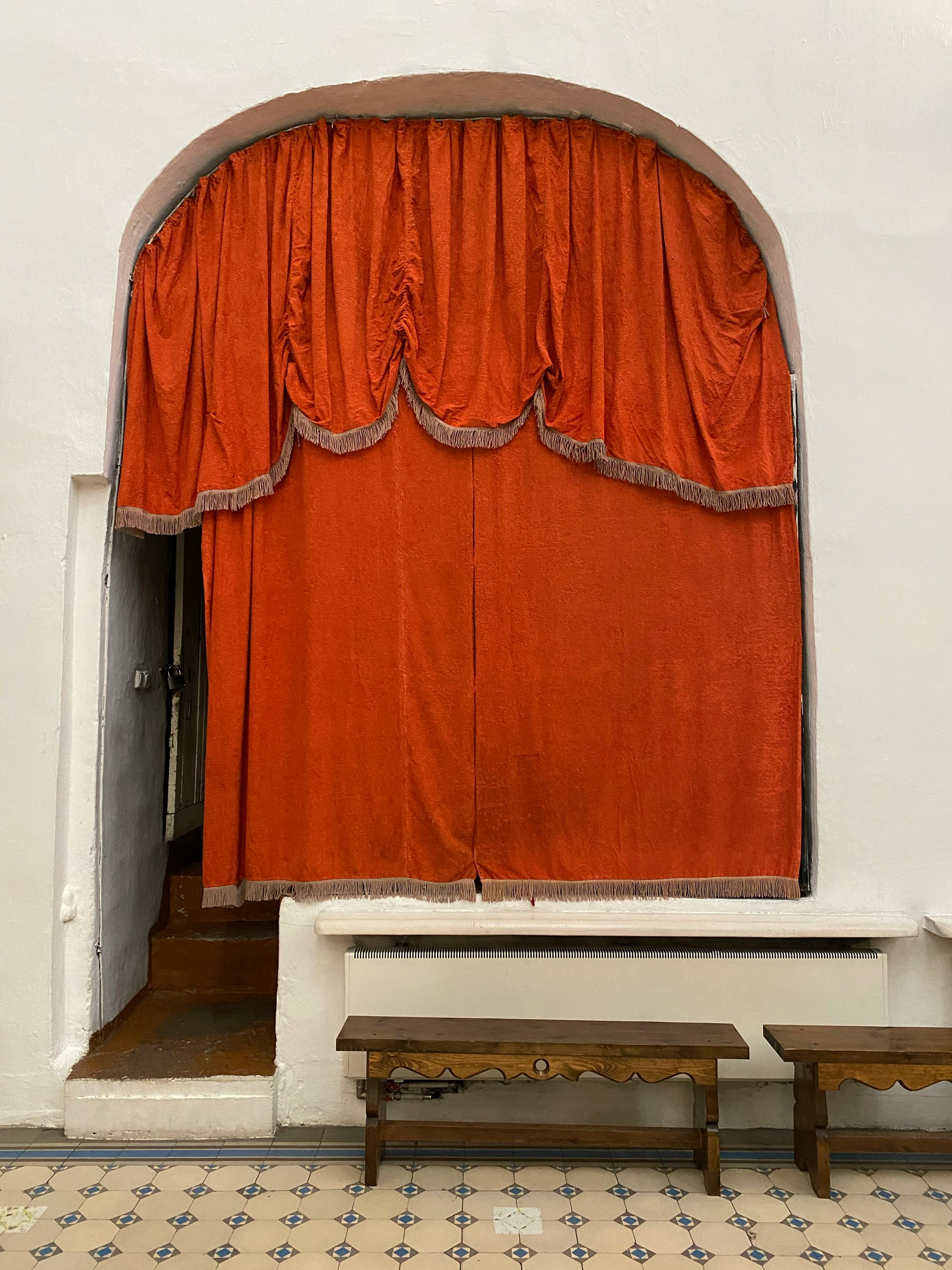 Elegant red curtain in an arched indoor setting with wooden benches.
