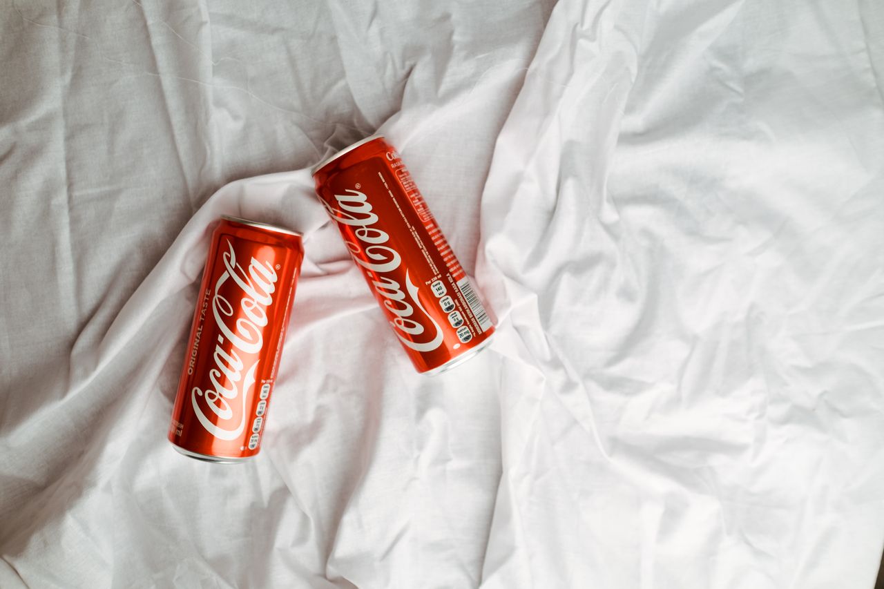 Two Coca Cola cans placed on a crumpled white textile, showcasing a classic beverage desig