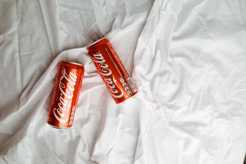 Free Two Coca Cola cans placed on a crumpled white textile, showcasing a classic beverage design. Stock Photo