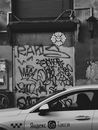 Grayscale Photo of Grafitti near a Sedan