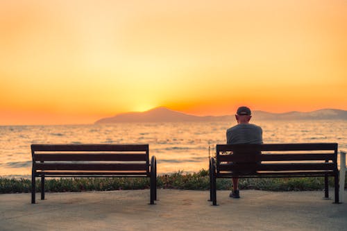 Free Man Sitting on Brown Wooden Bench Near the Sea Stock Photo