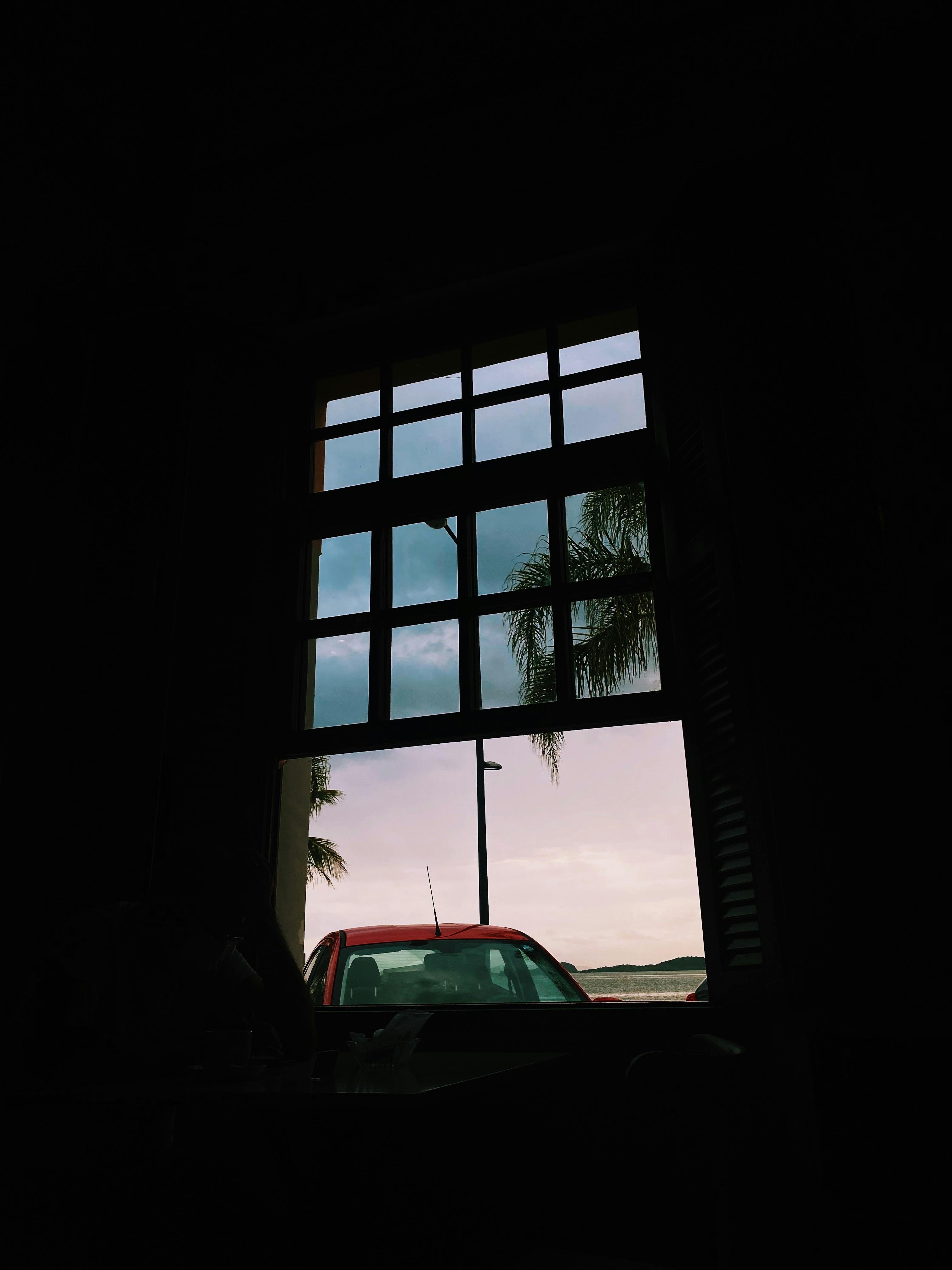 View of a red car and sky through a window at dusk in São Francisco do Sul, Brazil.