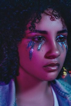 Close-up portrait of a woman with glitter makeup under vibrant lighting.