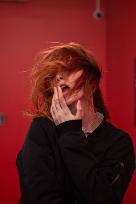 Dynamic studio portrait of a woman with flowing red hair and a hand on her lips, capturing a sense of mystery and allure.